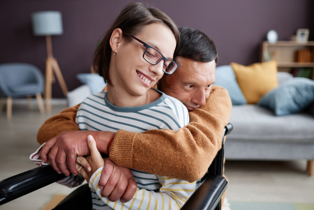 Un père attentionné embrasse une fille handicapée souriante à la maison